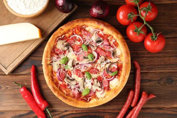 Lezzetli pizza, füme sosis ve ahşap masada malzemeler.