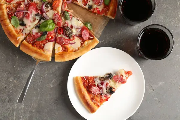 Gri masada servis edilen ince tütsülenmiş sosisli lezzetli bir pizza.