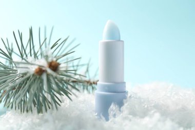 Nemlendirici dudak kremi ve yapay kar üzerindeki köknar ağacı dalları açık mavi arka planda, yakın plan. Kış bakımı