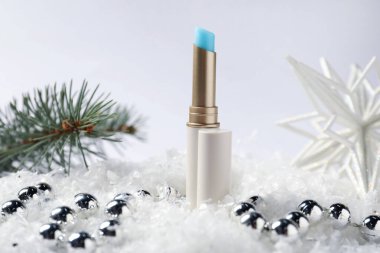 Nemlendirici dudak kremi, Noel dekorasyonu ve beyaz arka planda suni kar üzerindeki köknar ağacı dalları, yakın plan. Kış bakımı