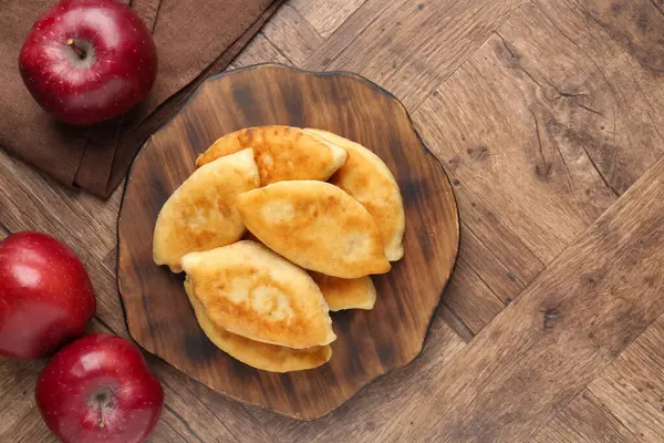 Lezzetli kızarmış pirizky (doldurulmuş turtalar) ve ahşap masa üzerinde elmalar, düz yatak. Metin için boşluk
