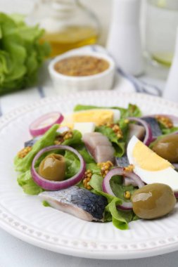 Ringa balıklı lezzetli salata, yumurta, hardal ve sebzeler beyaz masada, yakın plan.