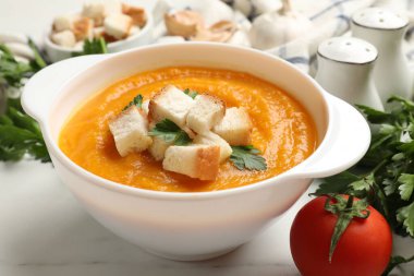 Beyaz mermer masa üzerinde maydanozlu ve domatesli balkabağı kremalı çorba, yakın plan.