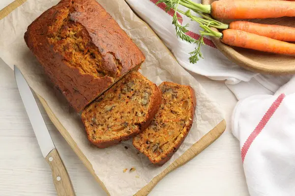 Beyaz ahşap masada fındıklı, sebzeli ve bıçaklı ev yapımı havuçlu kek.