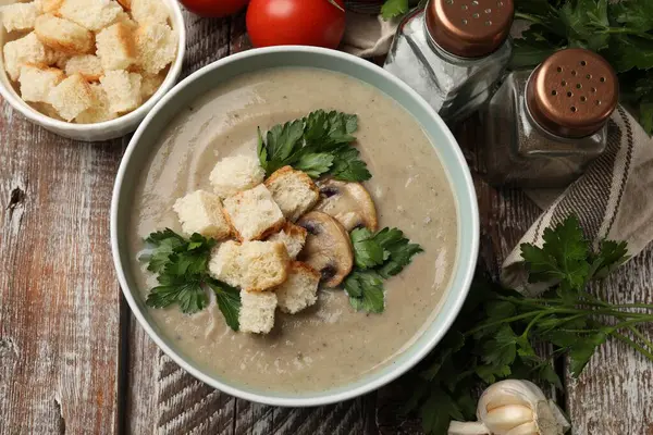 Lezzetli mantar kremalı çorba, kızarmış ekmek, maydanoz ve ahşap masa üzerindeki malzemeler.