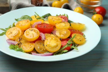 Açık mavi ahşap masada sarı domatesli taze salata, yakın plan.