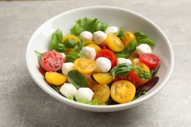 Sarı domatesli lezzetli salata, fesleğen ve mozzarella peyniri açık gri masada, yakın plan.