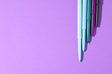 Mor arka planda renkli göz kalemleri, düz yatış. Metin için boşluk