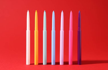 Kırmızı arkaplanda renkli göz kalemleri, yakın plan