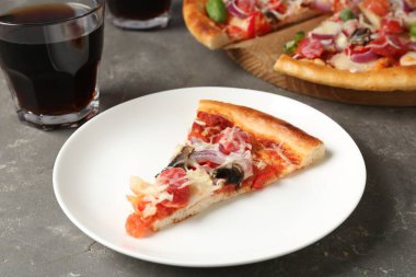 Gri masada servis edilen ince tütsülenmiş sosisli, lezzetli bir pizza.