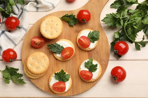 Krem peynirli krakerler, domatesler ve maydanozlar beyaz ahşap masada, düz yatıyordu.