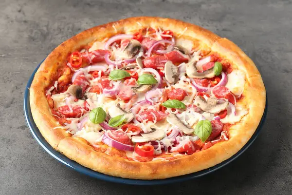 Gri desenli masada füme sosisli ve mantarlı lezzetli pizza, yakın plan.