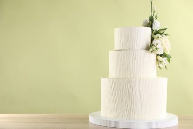 Ahşap masadaki çiçeklerle süslenmiş nefis bir düğün pastası açık yeşil arka planda, yakın plan. Metin için boşluk