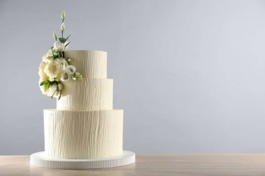 Gri arka planda, ahşap masada çiçeklerle süslenmiş lezzetli düğün pastası. Metin için boşluk