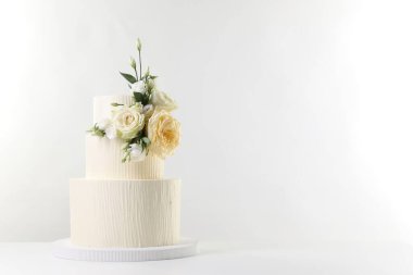 Masada beyaz arka planda çiçeklerle süslenmiş nefis bir düğün pastası. Metin için boşluk