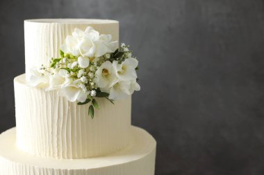 Gri arka planda çiçek dekoru olan lezzetli düğün pastası, yakın plan. Metin için boşluk