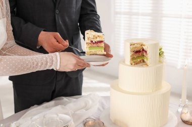 Damat, düğün pastasından bir parça tabağa koyuyor. Gelini masada kapalı tutuyor, yakın plan.