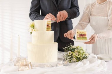 Yeni evliler kapalı bir masada düğün pastası kesiyorlar.