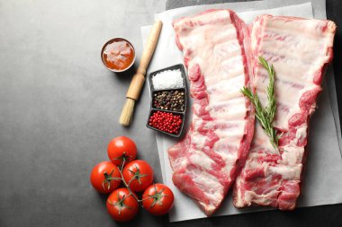 Çiğ domuz kaburgası, domates ve baharatlar gri masada, düz yerde.