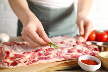 Kadın, masada çiğ domuz kaburgalarının üzerine biberiye koyuyor.