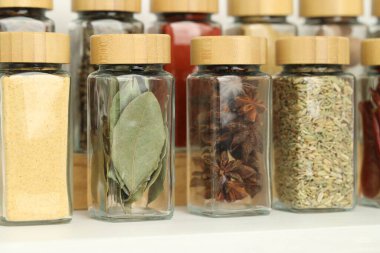 Beyaz masadaki kavanozlardaki farklı aromatik baharatlar, yakın plan.