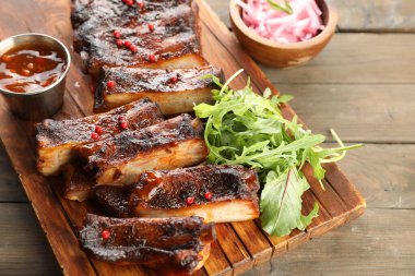 Lezzetli domuz pirzolası, roka, sos ve soğan ahşap masada, yakın plan.