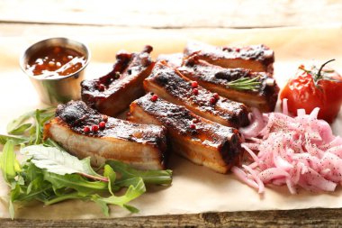 Lezzetli domuz kaburgası, sos, roka ve soğan ahşap masada, yakın plan.