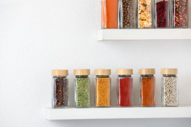 Beyaz raflardaki kavanozlardaki farklı aromatik baharatlar.