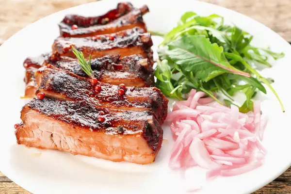 Lezzetli pirzola, soğan ve roka ahşap masada, yakın plan.