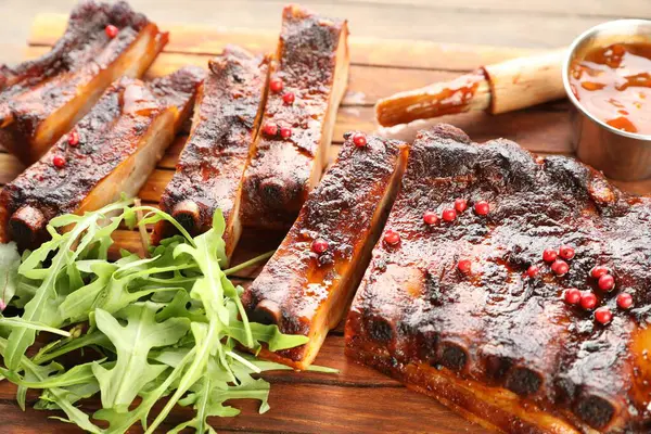 Lezzetli domuz pirzolası, roka, sos ve soğan ahşap masada, yakın plan.