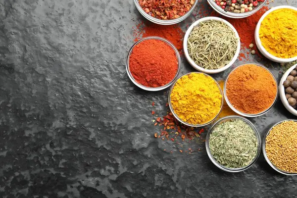 Tabaklardaki farklı aromatik baharatlar karanlık masada, düz yerde. Metin için boşluk