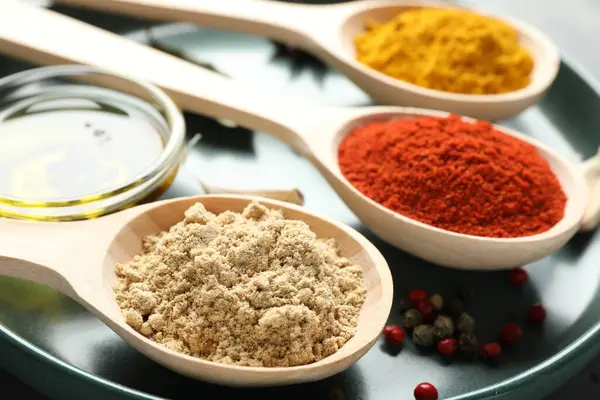 Gri masadaki kaşıklardaki farklı baharatlar, yakın plan.