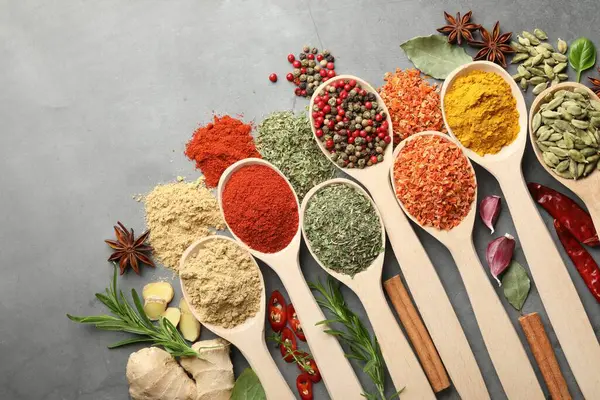 Gri masadaki kaşıklardaki farklı baharatlar düzdü.