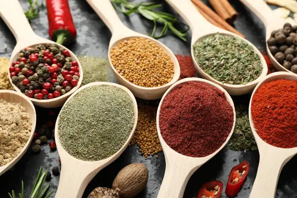 Gri masadaki kaşıklardaki farklı baharatlar, yakın plan.