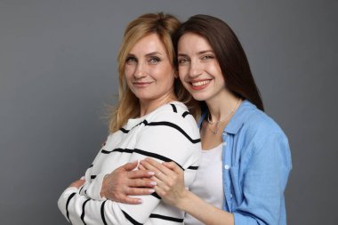 Anne ve kızı gri arka planda sarılıyorlar.