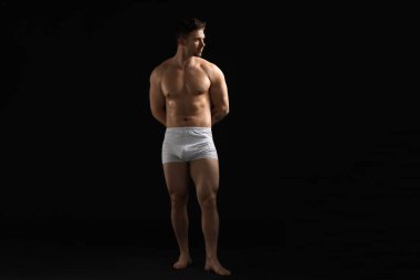 Siyah arka planda beyaz iç çamaşırlı genç bir adam.