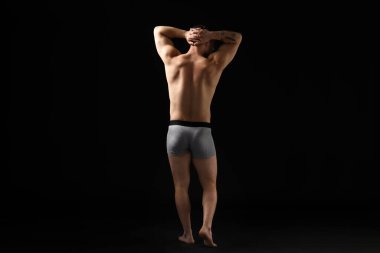 Siyah arka planda açık gri iç çamaşırlı genç adam.