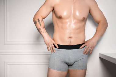 Beyaz duvarın yanında şık açık gri iç çamaşırlı genç adam, yakın plan.