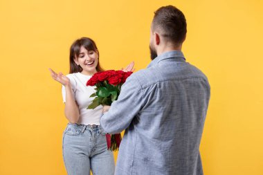 Adam turuncu arka planda sevgilisine kırmızı gül buketi sunuyor.