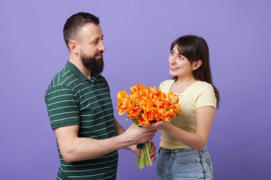 Adam mor arka planda sevgili karısına kırmızı güller sunuyor.