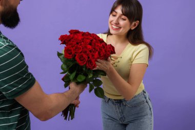 Mor arka planda sevgilisine kırmızı güller sunan bir adam, yakın plan.