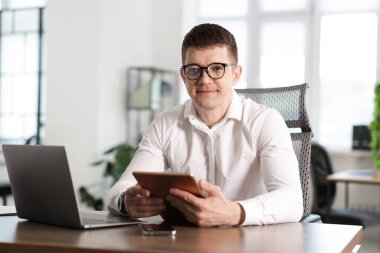 Ofiste çalışan tabletli ve laptoplu bir adam.