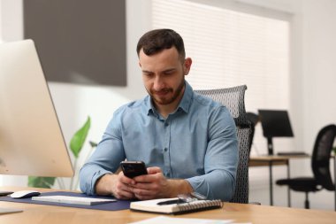 Ofiste çalışırken akıllı telefon kullanan bir adam.