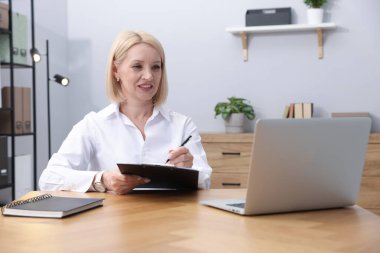 Ofiste dizüstü bilgisayarla çalışırken not alan profesyonel bir psikolog.