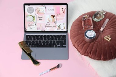 Güzellik blogu siteli dizüstü bilgisayar, parfümler ve pembe arka planda farklı aksesuarlar.