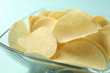Açık mavi arka planda leziz patates cipsi, yakın plan.