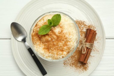 Tarçınlı leziz pirinç pudingi, beyaz ahşap masada nane ve kaşık, üst manzara.