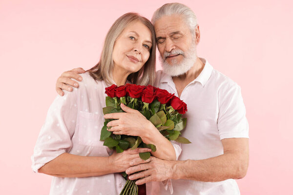 Lovely couple with bouquet of red roses on pink background