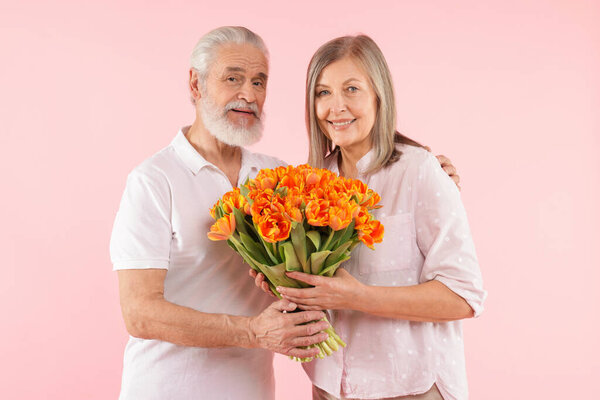 Happy couple with bouquet of tulips on pink background