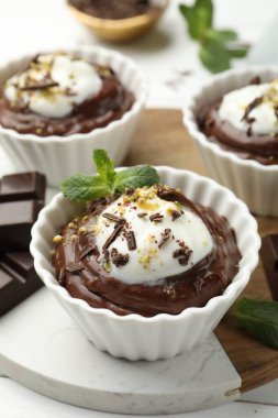 Krem şantili lezzetli puding ve beyaz ahşap masadaki çikolata parçaları, yakın plan.